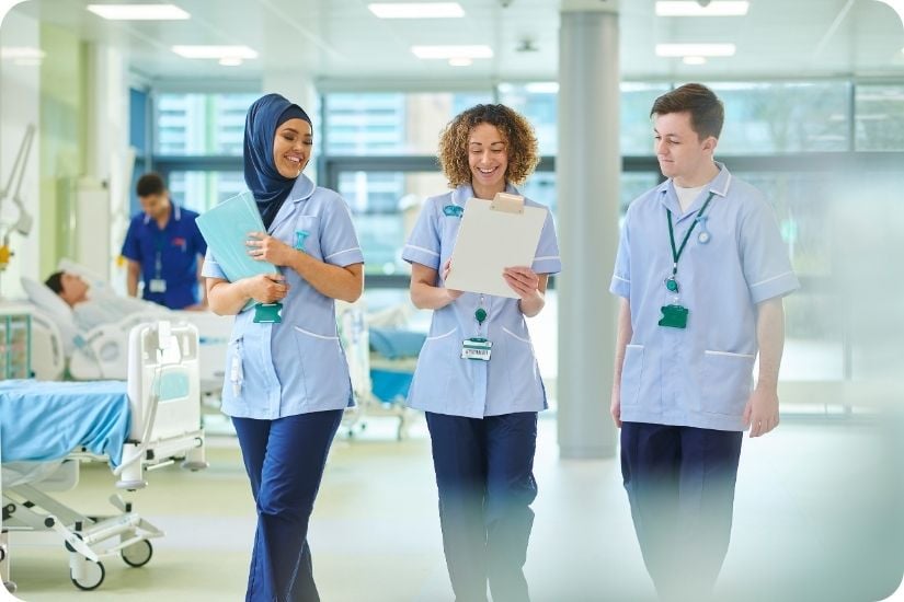 Drei junge Pflegekräfte gehen im Gespräch durch einen Klinikflur